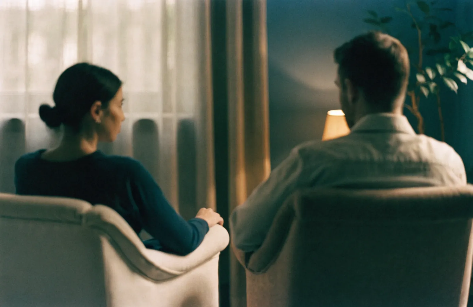 Two people sitting in armchairs in a softly lit room, in unhurried conversation